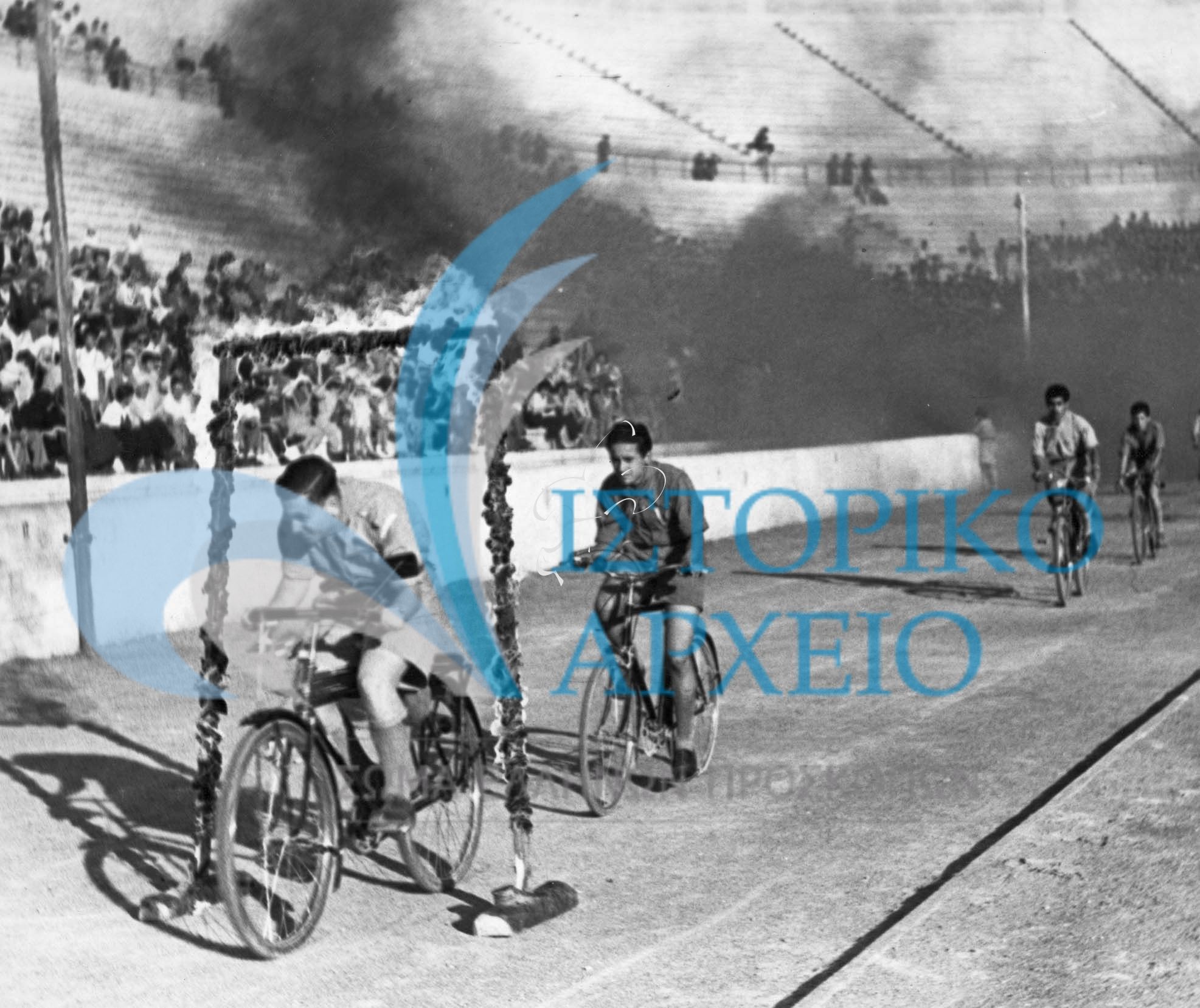 Πρόσκοποι ποδηλάτες διέρχονται από φλεγόμενη πύλη κατά την προσκοπική επίδειξη του Τοπικού Προσκοπικού Συνδέσμου Αθηνών στο Στάδιο το 1949.