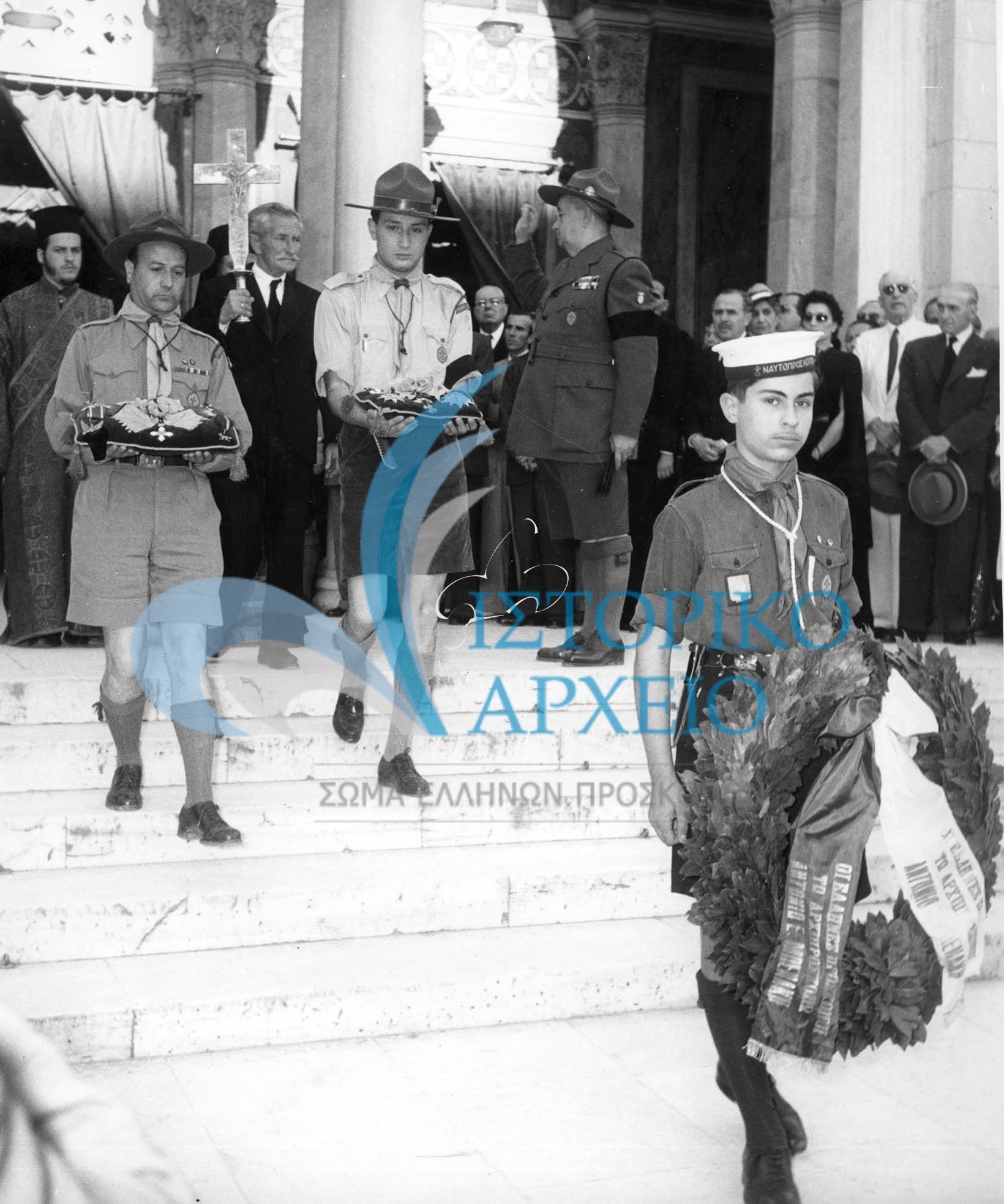 Πρόσκοποι μεταφέρουν τους μεγαλόσταυρους και τα παράσημα στην κηδεία του Αρχιπροσκόπου Αντώνη Μπενάκη το 1954. Διακρίνεται σε μικρή ηλικία ο Ι. Χαρίτος.