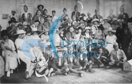 Οι πρόσκοποι της Σμύρνης μετά την συμμετοχή στον έρανο υπέρ του Ελληνικού Ερυθρού Σταυρού το 1920. Καθισμένος στη μέση ο Ε. Ιωαννίδης και πίσω του ο περιφερειακός έφορος Δ. Δάλλας. Γύρω από το τραπέζι οι κυρίες της ερανικής επιτροπής του Ερυθρού Σταυρού.