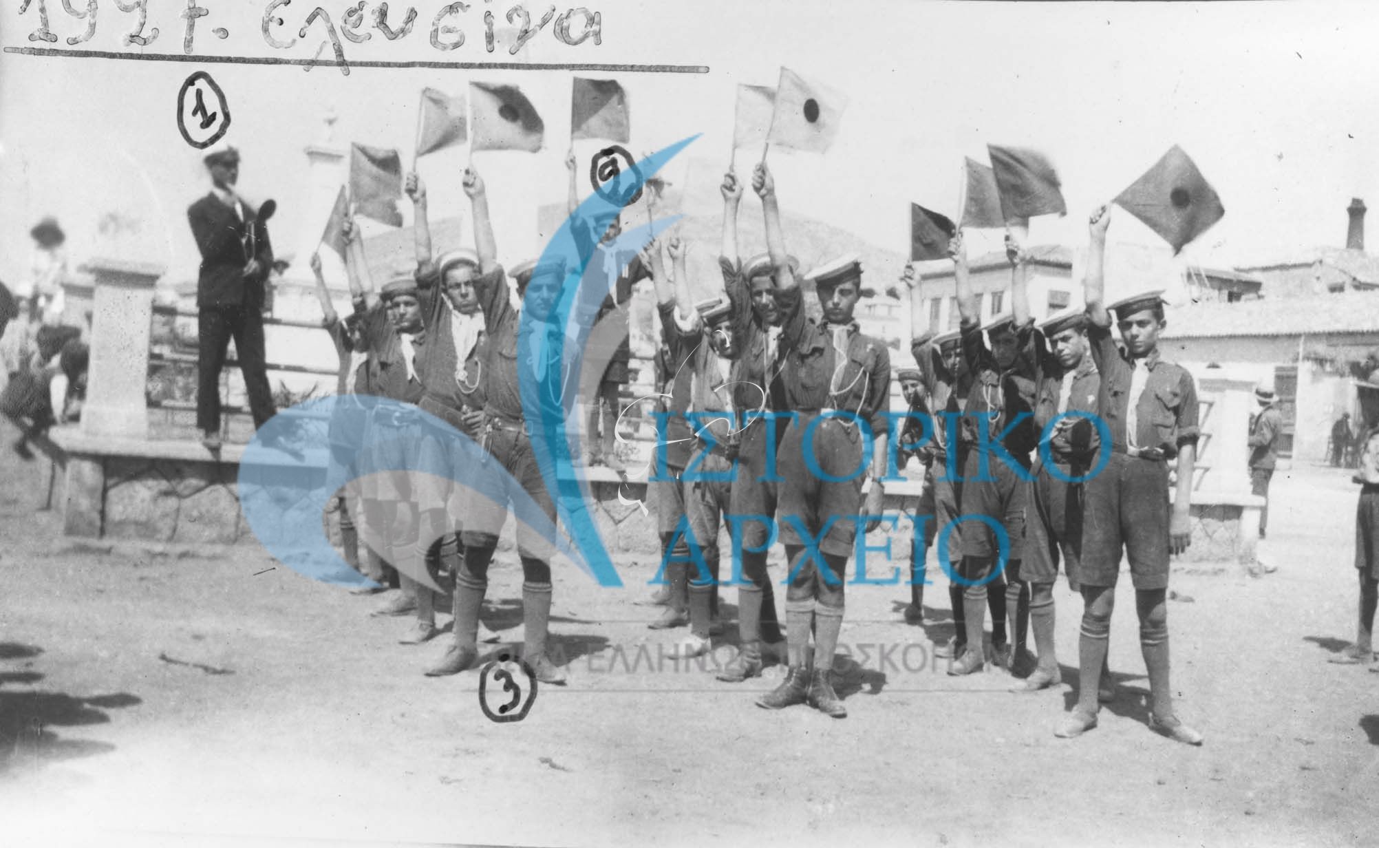 Πρόσκοποι Νίκαιας σε ασκήσεις δια βραχιόνιας επικοινωνίας με το Σύστημα Μορς στην Κεντρική Πλατεία Ελευσίνα κατά τη διάρκεια εκδρομής το 1927. Διακρίνονται: 1. Μανώλης Βελισσάριος,2. Σ Τερκεσίδης 3.Κ Λουίζος