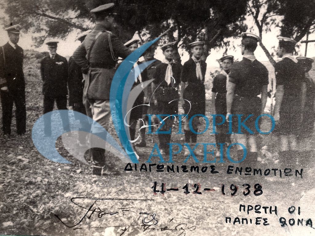 Επίσκεψη του Διαδόχου Παύλου  στο Διαγωνισμό Ενωμοτιών τον Δεκέμβριο του 1938, εδώ με την νικήτρια Ενωμοτία της 9ης Αθηνών. Διακρίνονται επίσης: Μ. Μίνδλερ, Α. Μπενάκης, Τ. Γκαζιάνης και Δ. Αλεξάτος. Η φωτογραφία περιέχει ιδιόχειρη υπογραφή του Διαδόχου.