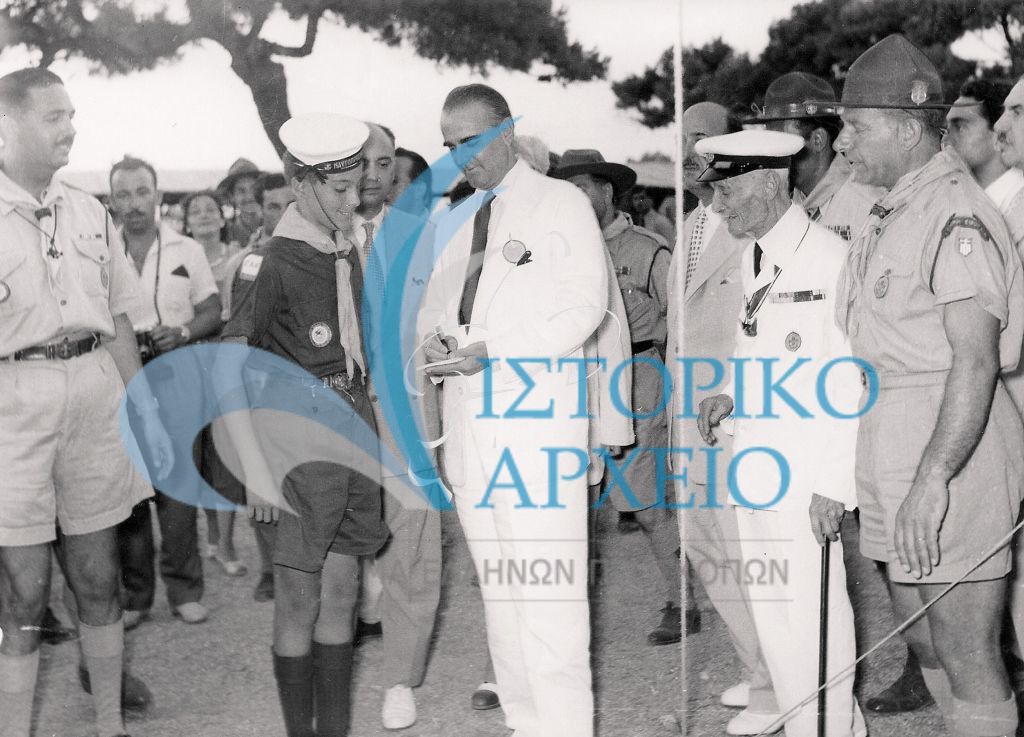 Ο Πρωθυπουργός Κωνσταντίνος Καραμανλής υπογράφει αφιέρωση σε απόδημο ναυτοπρόσκοπο στο Τζάμπορη του Αγίου Ανδρέα το 1956. Διακρίνεται ο Μ. Σοφιανός και Σκυριανίδης.