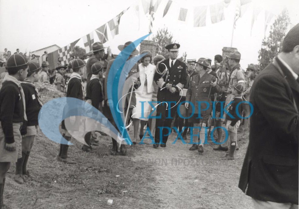 Λυκόπουλα και πρόσκοποι υποδέχονται τον Βασιλιά Κωνσταντίνο με την Βασίλισσα Άννα Μαρία που συνοδεύονται από τον ΓΕ Δ. Αλεξάτο στα εγκαίνια του Νεώσοικου της Θεσσαλονίκης το 1964.