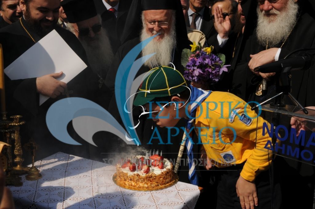 Λυκόπουλο της Μυτιλήνης που γεννήθηκε την ίδια ημερομηνία με τον Οικουμενικό Πατριάρχη σβήνει τα κεράκια της τούρτας γενεθλίων τους κατά τα εγκαίνια του Προσκοπικού Κέντρου Περιβαλλοντικής Εκπαίδευσης στον Ασώματο Λέσβου το 2009.