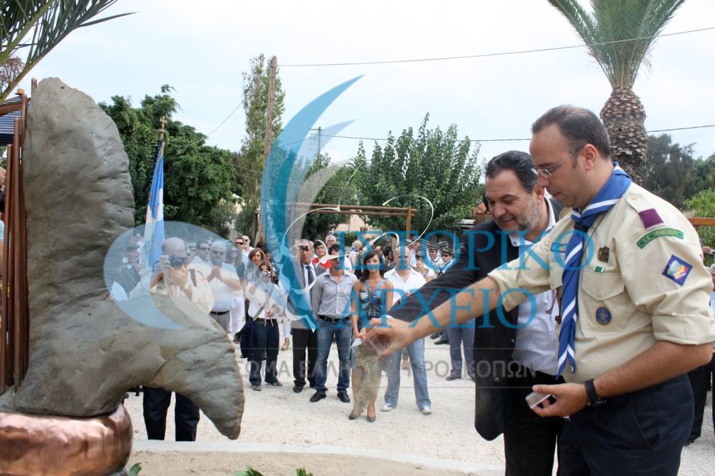 Ο Δήμαρχος Ηρακλείου Ι. Κουράκης και ο ΠΕ Ηρακλείου Μ. Απλαδενάκης θέτουν χώμα από τον ποταμό Εύδωνα (τόπος μαρτυρίου των προσκόπων Αϊδινίου) κατά τα αποκαλυπτήρια του Μνημείου Πεσόντων Ελλήνων Προσκόπων Μικράς Ασίας στο Ηράκλειο το 2009. Όρθια μπροστά διακρίνεται η σχεδιάστρια του μνημείου Ευρ. Λεκάκη.