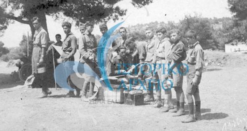 Πρόσκοποι της 3ης Ομάδας Αθηνών περιμένουν στη σειρά για να γεμίσουν τα σκεύη τους με το μεσημεριανό φαγητό στην κατασκήνωση στο Διόνυσο Αττικής Δεκαπενταύγουστου του 1925.