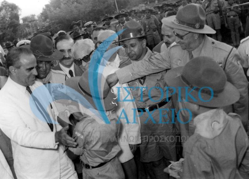 Ο Πρωθυπουργός Κωνσταντίνος Καραμανλής συνομιλεί με πρόσκοπο κατά την επίσκεψή του στην Πυρά Έναρξης του Πανελληνίου Τζάμπορη Αποδήμων Ελλήνων Προσκόπων το 1956.