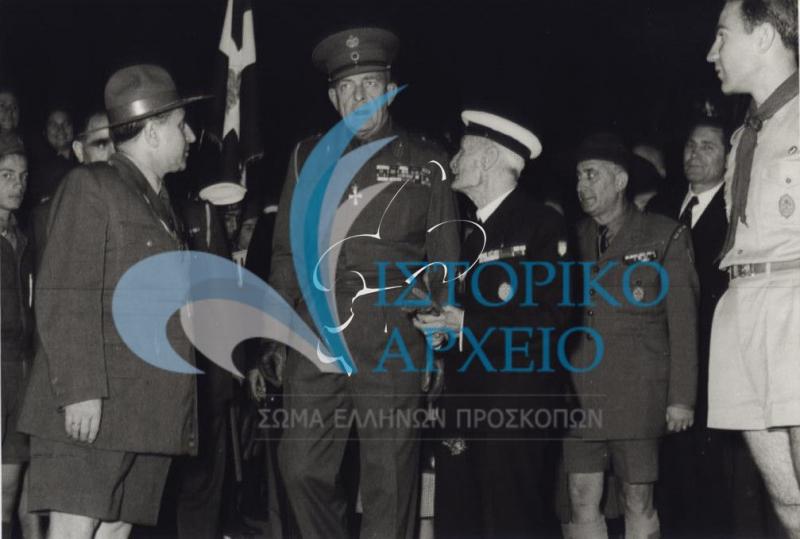 Πρόσκοποι και Βαθμοφόροι υποδέχονται τον Βασιλιά Παύλο στην επίσκεψή του Βασιλικού Ζεύγους στην Περιφέρεια Θεσσαλονίκης το 1957. Διακρίνονται ο έφορος Θεσσαλονίκης Δ. Μακρίδης, ο Πρόεδρος ΔΣ Σοφιανός και ο ΓΕ Δ. Αλεξάτος.
