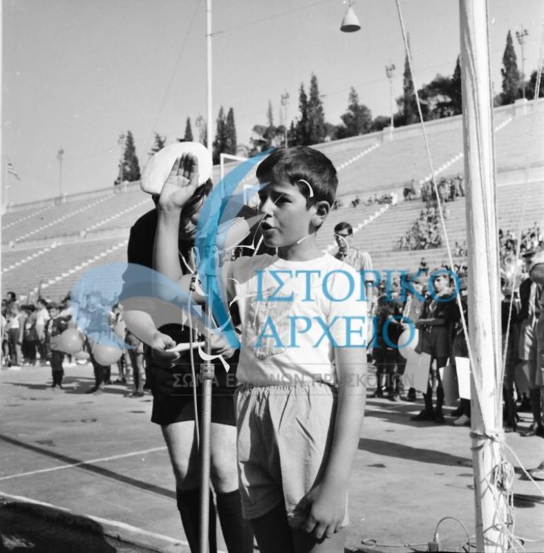 Στιγμιότυπο από του Πανελλήνιους Αγώνες Λυκοπούλων το 1966 στο Στάδιο κατά την εκφώνηση του όρκου του αθλητή. Δίπλα στο λυκόπουλο διακρίνεται ο Π. Δάνδολος.