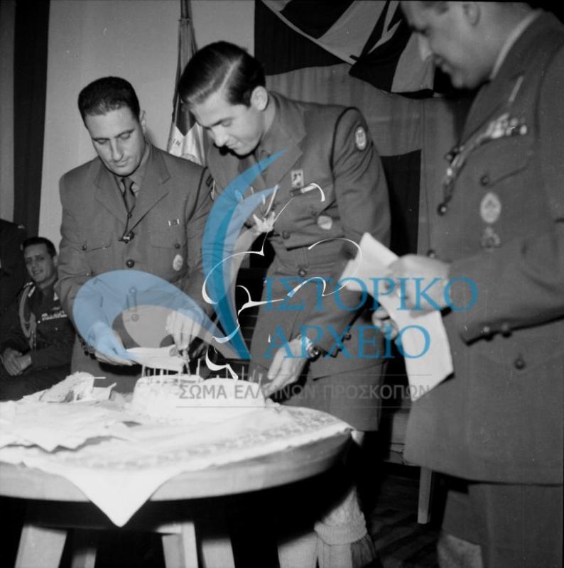 Ο Διάδοχος Κωνσταντίνος στην κοπή της βασιλόπιτας του ΣΕΠ το 1961, μετά την απονομή του μαντηλίου "Προσκόπος Βασιλέως". Διακρίνονται ο ΓΕ Δ. Αλεξάτος και ο Α. Κωνσταντόγλου.