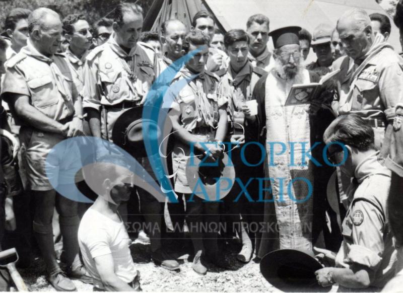 Ιερέας απευθύνει δέηση κατά την θεμελίωση του προσκοπικού καταφυγίου στην Αμφίκλεια μετά την έναρξη του Τζάμπορη Ιωβηλαίου το 1960. Διακρίνεται ο Διάδοχος Κωνσταντίνος με στολή και ο ΓΕ Δ. Αλεξάτος.