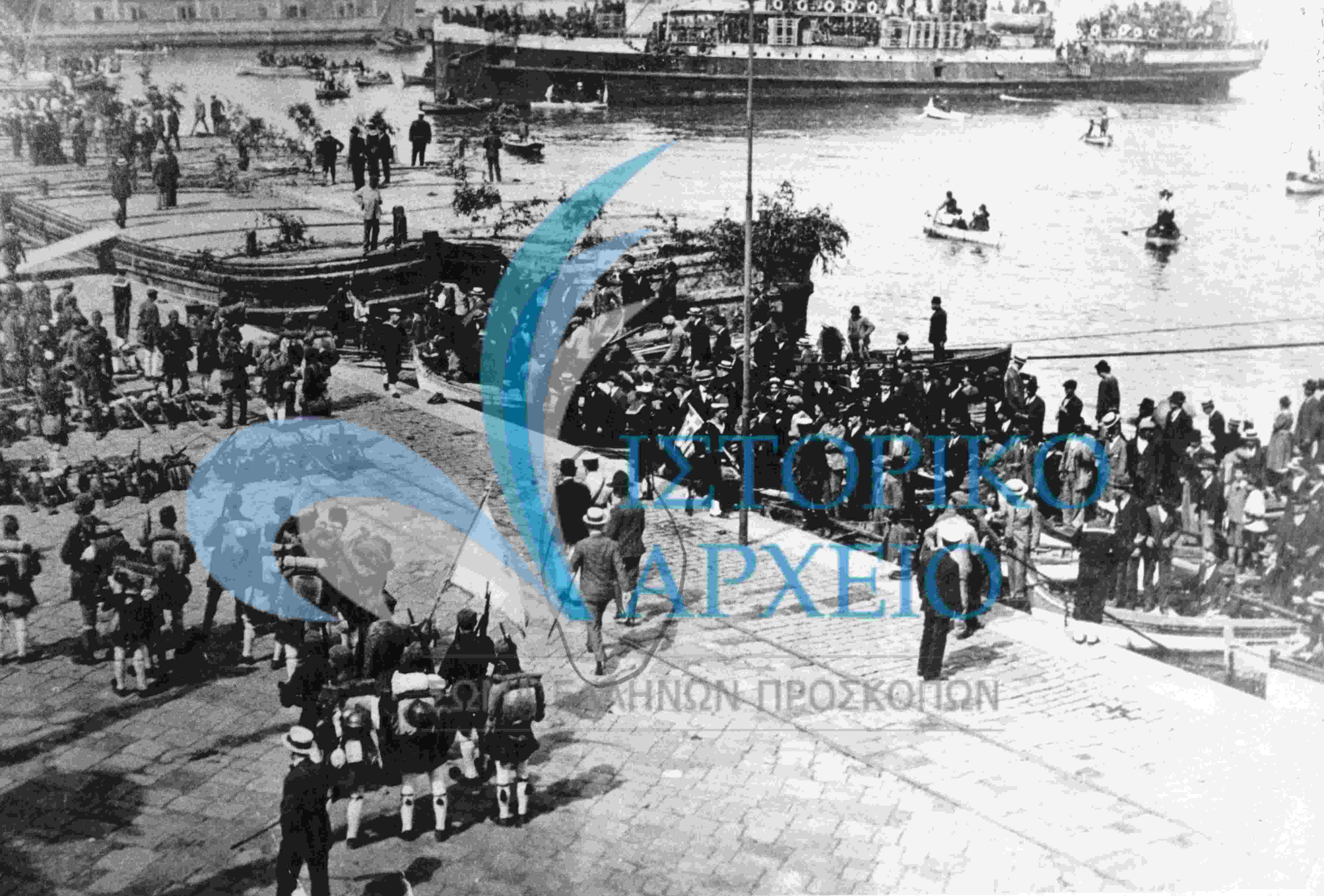 Ο Ελληνικός Στρατός, κρατώντας ελληνική σημαία, αποβιβάζεται στη Σμύρνη στις 2 Μαΐου 1919. Στον κύκλο ο Αρχηγός των Ελλήνων Προσκόπων Σμύρνης υποδέχεται τον αξιωματικό στην προκυμαία.