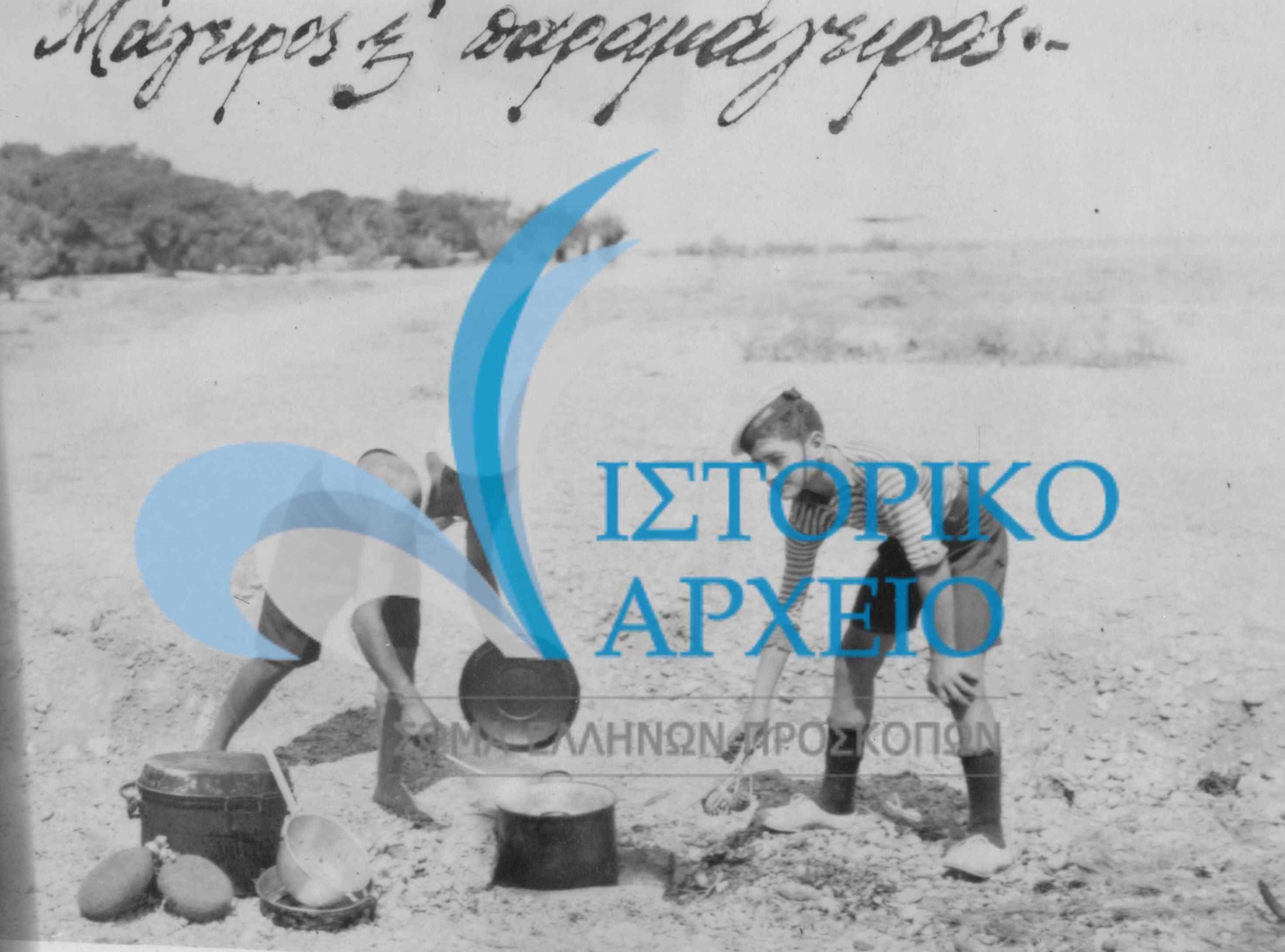Ο μάγειρας και ο παραμάγειρας της κατασκήνωσης του 1ου Ν/Π Κορίνθου στην προετοιμασία του φαγητού δίπλα στη θάλασσα στα Πεύκα Ξυλοκάστρου το 1935.