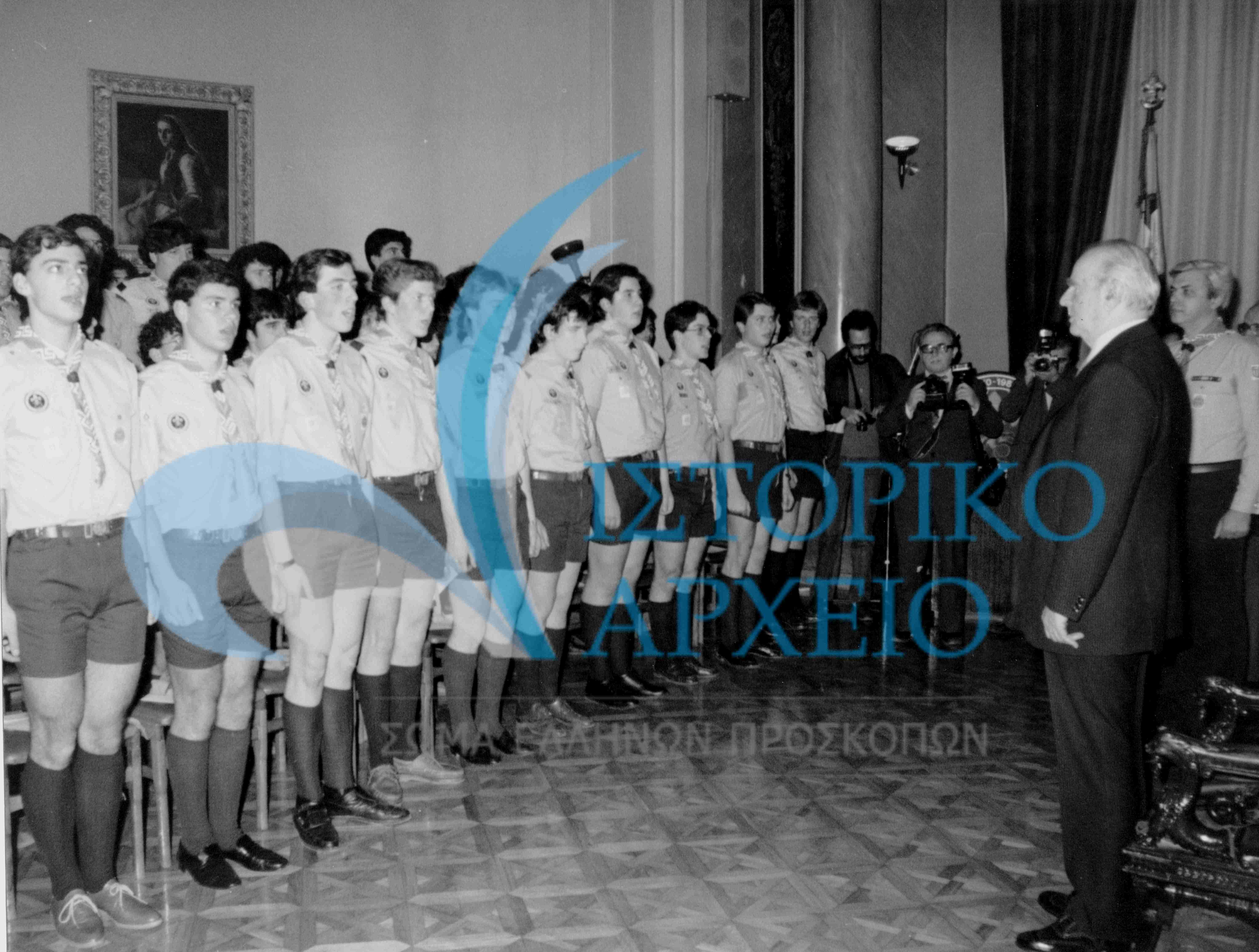 Οι Πρόσκοποι Έθνους μετά την επίδοση του μαντηλιού τους, τραγουδούν τον Εθνικό Ύμνο μπροστά από τον Πρόεδρο της Δημοκρατίας Κων. Καραμανλή το 1980.