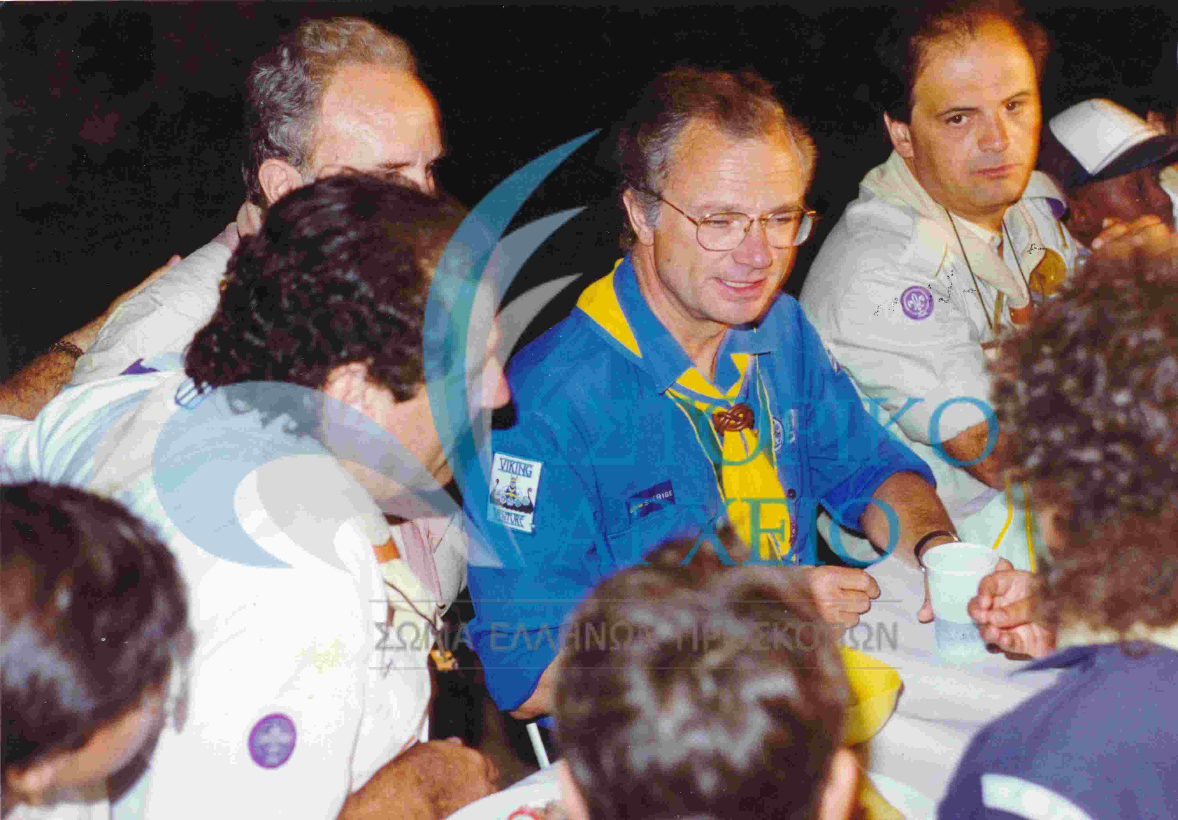 Ο Βασιλιάς της Σουηδίας Κάρολος Γουστάβος στο δείπνο που προσφέρθηκε στην κατασκήνωση των στελεχών της ΕΠ Κρήτης κατά τη διάρκεια της επίσκεψης στον Αγ. Νικόλαο για τη συνάντηση των μελών του Παγκοσμίου Ιδρύματος BP Fellows το 1993. Διακρίνεται ο Στ. Κοκκίνης ΠΕ Χανίων κι ο Γ. Χουρδάκης
