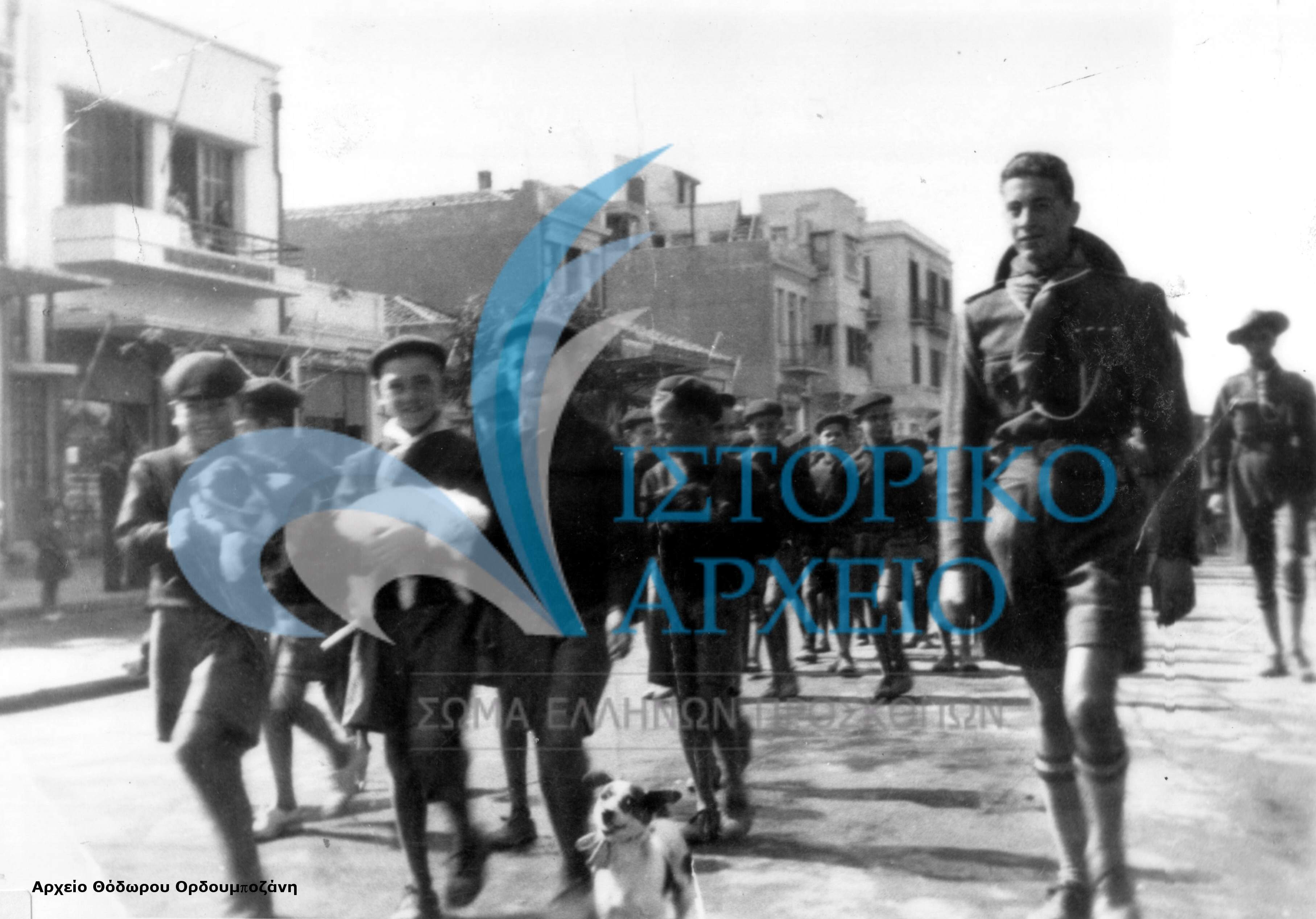 Τα λυκόπουλα της 2ης Αγέλης Αλεξανδρούπολης κρατώντας ζωάκια στα χέρια, μαζί με τον Αρχηγό τους Αργύρη Καλογήρου και τον Υπαρχηγό Χαχαμίδη, κατευθύνονται στο χώρο της πλατείας του Σιδηροδρομικού Σταθμού, όπου θα γιορτάσουν τη γιορτή των ζώων τον Οκτώβριο του 1938.