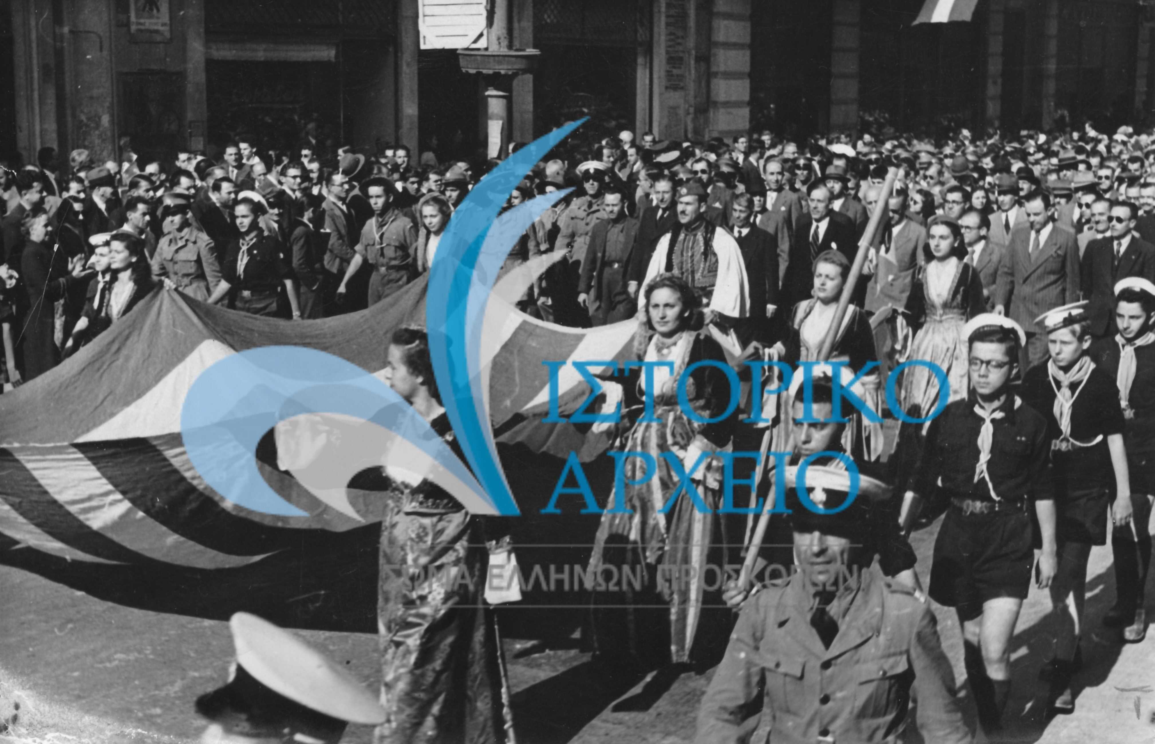 Πρόσκοποι και κοπέλες του Λυκείου Ελληνίδων στην οδό Μητροπόλεως κατά τους εορτασμούς για την Απελευθέρωση των Αθηνών από τα στρατεύματα κατοχής το 1946. Την πομπή ακολουθεί ο Δήμαρχος Αθηναίων Αριστείδης Σκληρός.